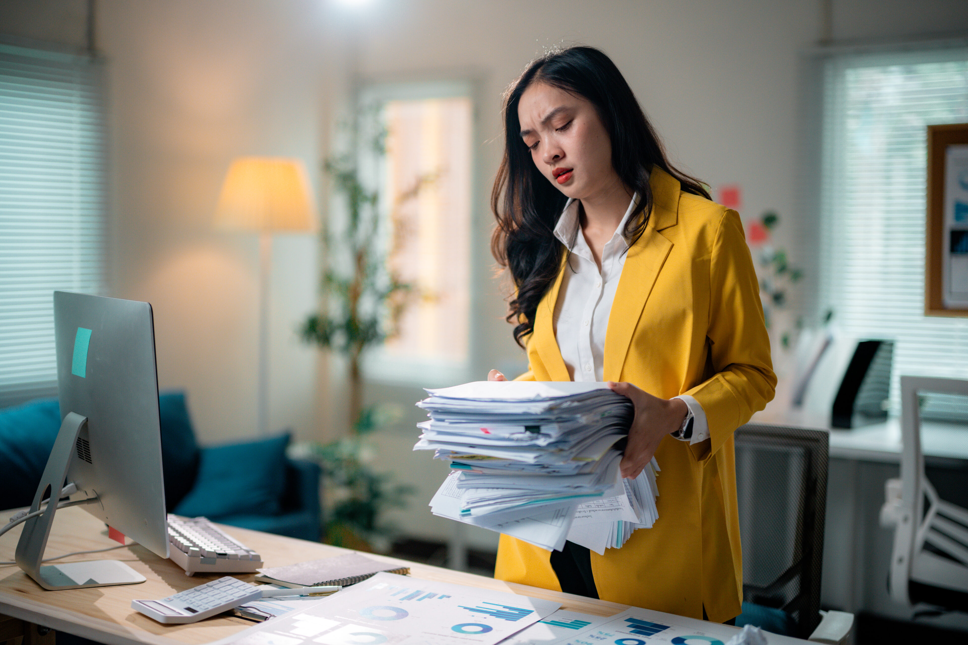 Young Asian businesswoman looking stressed while carrying a large stack of paperwork in a modern office