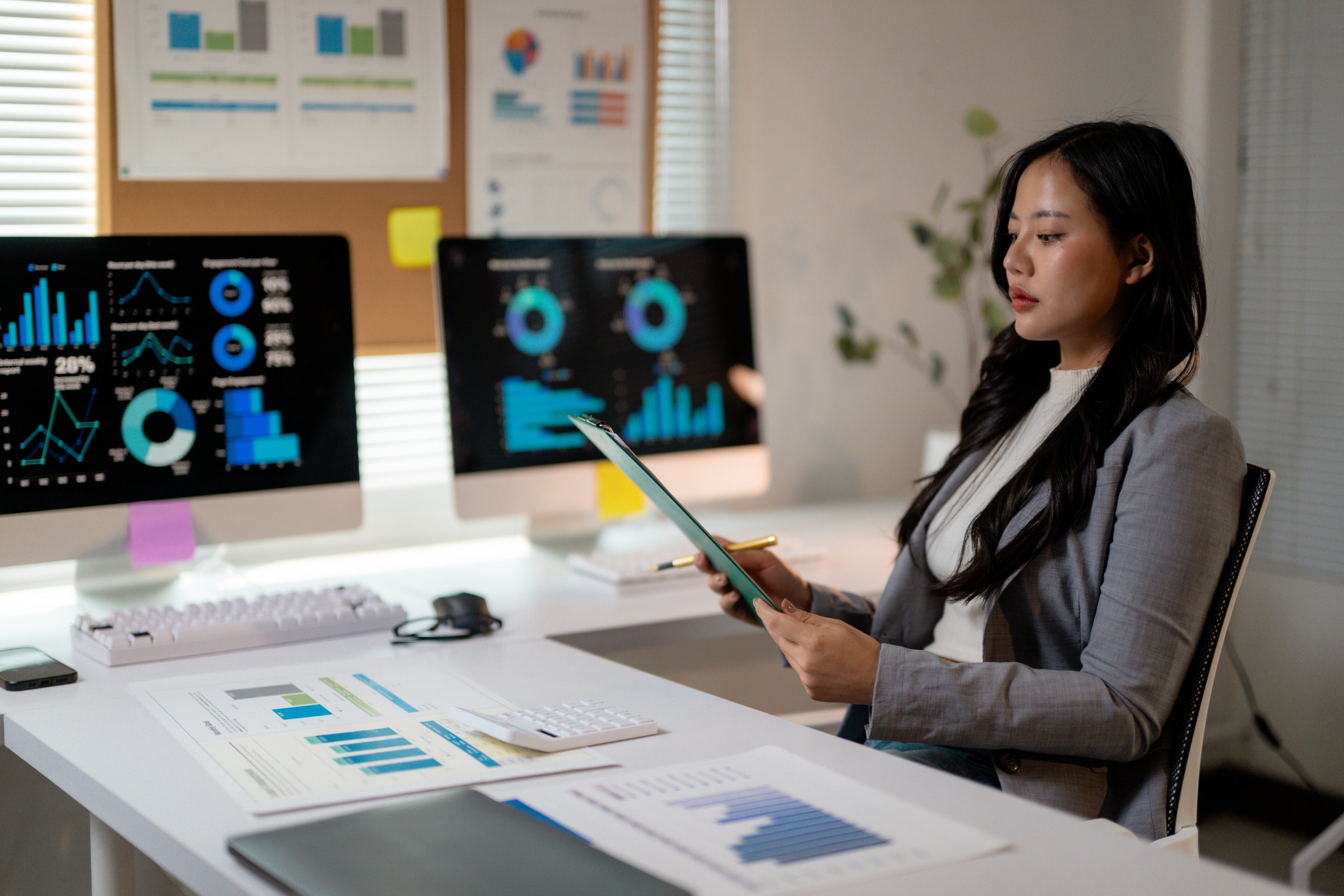 Professional analyzing financial reports on multiple monitors, displaying corporate workspace with sleek technology